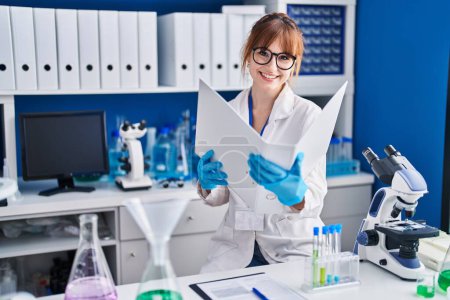 Photo for Young woman scientist smiling confident reading report at laboratory - Royalty Free Image