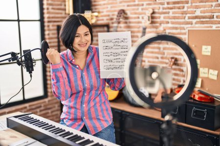 Photo for Young asian woman doing online music tutorial showing music sheet screaming proud, celebrating victory and success very excited with raised arm - Royalty Free Image
