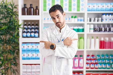 Photo for Handsome hispanic man working at pharmacy drugstore pointing to both sides with fingers, different direction disagree - Royalty Free Image