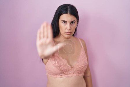 Téléchargez les photos : Jeune femme hispanique portant un soutien-gorge rose faire arrêter chanter avec la paume de la main. expression d'avertissement avec geste négatif et sérieux sur le visage. - en image libre de droit