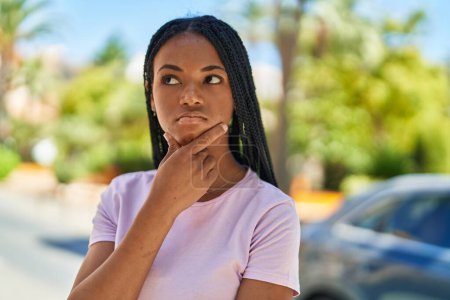 Téléchargez les photos : Femme afro-américaine debout avec l'expression du doute au parc - en image libre de droit