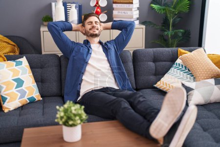 Téléchargez les photos : Young caucasian man relaxed with hands on head sitting on sofa at home - en image libre de droit