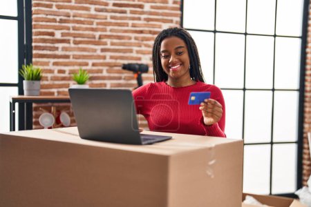 Foto de Mujer afroamericana sonriendo confiada usando laptop y tarjeta de crédito en nuevo hogar - Imagen libre de derechos