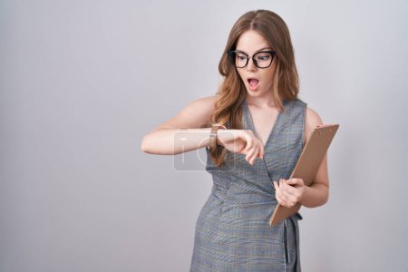 Téléchargez les photos : Femme caucasienne portant des lunettes et des vêtements de travail en regardant le temps de la montre inquiet, peur de se tard - en image libre de droit