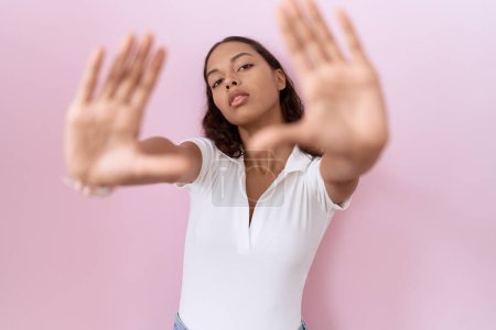 Téléchargez les photos : Jeune femme hispanique portant un t-shirt blanc décontracté faisant cadre en utilisant les mains, les paumes et les doigts, perspective de la caméra - en image libre de droit
