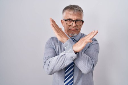 Foto de Hombre de negocios hispano con cabello gris usando gafas expresión de rechazo cruzando brazos haciendo signo negativo, cara enojada - Imagen libre de derechos