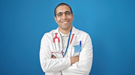 Photo for Young hispanic man doctor smiling confident standing with arms crossed gesture over isolated blue background - Royalty Free Image