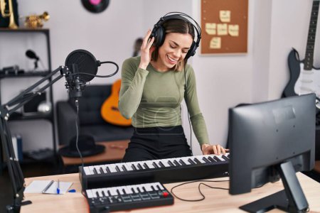 Foto de Young beautiful hispanic woman musician smiling confident playing piano at music studio - Imagen libre de derechos
