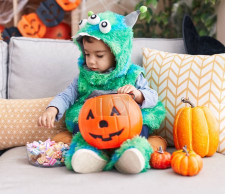 Téléchargez les photos : Adorable garçon hispanique ayant fête d'Halloween tenant des bonbons à la maison - en image libre de droit