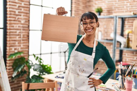 Photo for Young beautiful hispanic woman artist smiling confident holding briefcase at art studio - Royalty Free Image