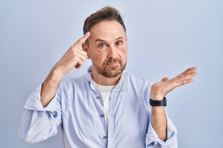 Photo for Middle age caucasian man standing over blue background confused and annoyed with open palm showing copy space and pointing finger to forehead. think about it. - Royalty Free Image