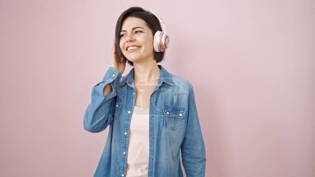 Téléchargez les photos : Jeune femme caucasienne écoutant de la musique portant des écouteurs sur fond rose isolé - en image libre de droit
