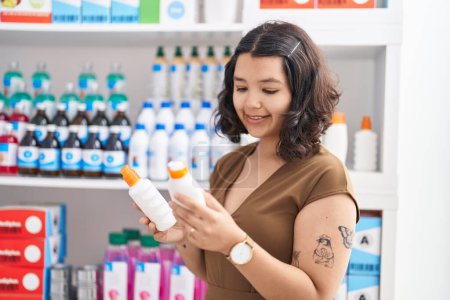 Photo for Young woman customer holding sunscreen bottles at pharmacy - Royalty Free Image