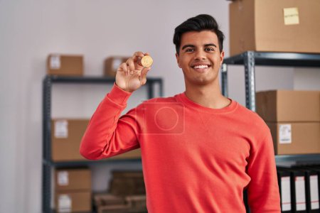 Téléchargez les photos : Homme hispanique travaillant à la petite entreprise commerce électronique tenant Bitcoin regardant positif et heureux debout et souriant avec un sourire confiant montrant dents - en image libre de droit