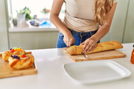 Foto de Joven hermosa mujer hispana preparando el desayuno cortando pan en la cocina - Imagen libre de derechos