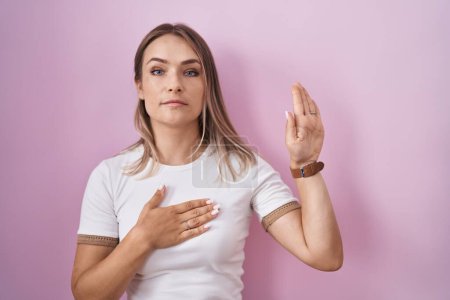 Photo for Blonde caucasian woman standing over pink background swearing with hand on chest and open palm, making a loyalty promise oath - Royalty Free Image