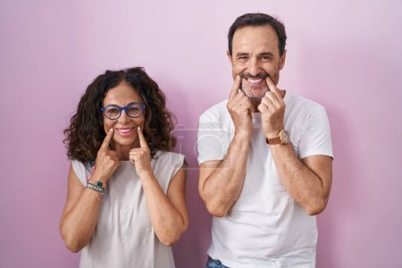 Téléchargez les photos : Couple hispanique du moyen âge ensemble sur fond rose souriant avec bouche ouverte, doigts pointant et forçant sourire joyeux - en image libre de droit
