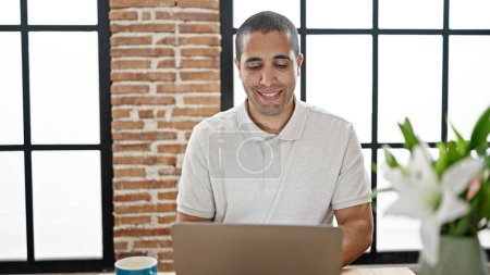 Téléchargez les photos : Jeune homme hispanique utilisant un ordinateur portable assis sur la table à la salle à manger - en image libre de droit