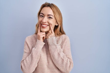 Téléchargez les photos : Femme hispanique debout sur fond bleu souriant avec la bouche ouverte, les doigts pointant et forçant sourire joyeux - en image libre de droit