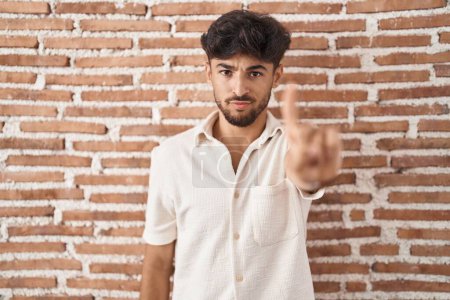 Téléchargez les photos : Homme arabe avec barbe debout sur le mur de briques arrière-plan pointant avec le doigt vers le haut et l'expression en colère, ne montrant aucun geste - en image libre de droit