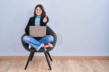 Téléchargez les photos : Jeune femme hispanique assis sur la chaise en utilisant ordinateur portable souriant joyeuse offrant main de paume donnant assistance et acceptation. - en image libre de droit