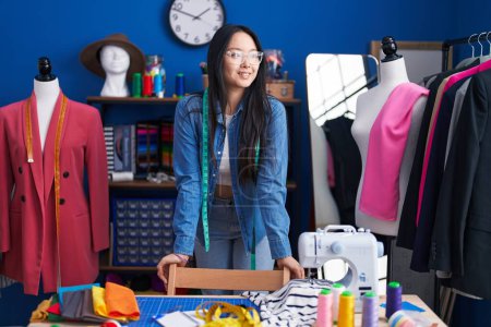 Téléchargez les photos : Jeune femme chinoise tailleur souriant confiance debout à l'usine de vêtements - en image libre de droit