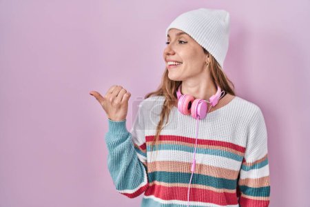 Photo for Young blonde woman standing over pink background smiling with happy face looking and pointing to the side with thumb up. - Royalty Free Image