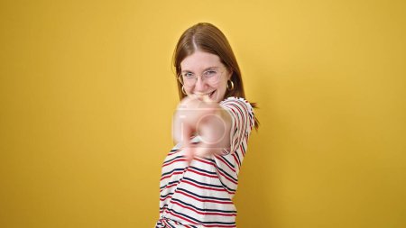 Foto de Mujer rubia joven sonriendo confiado señalando a la cámara sobre el fondo amarillo aislado - Imagen libre de derechos