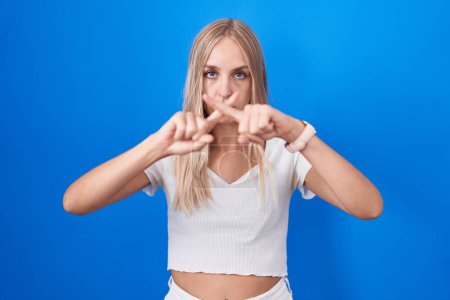 Téléchargez les photos : Jeune femme caucasienne debout sur fond bleu expression de rejet croisant les doigts faisant signe négatif - en image libre de droit