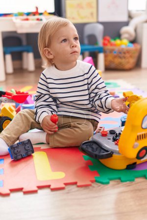 Foto de Adorable chico caucásico jugando con herramientas juguete sentado en el suelo en el jardín de infantes - Imagen libre de derechos