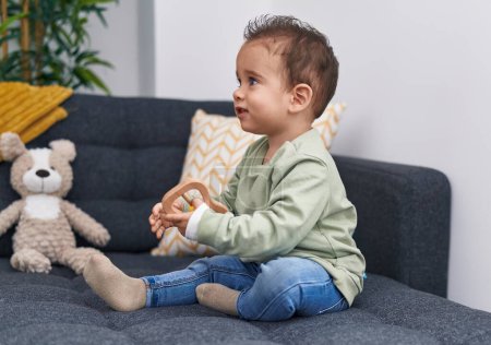 Photo for Adorable hispanic boy playing with toy sitting on sofa at home - Royalty Free Image