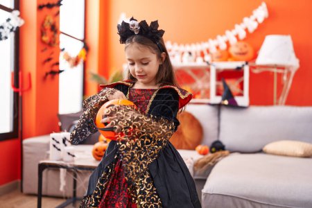 Foto de Adorable chica hispana con disfraz de halloween sosteniendo canasta de calabaza en casa - Imagen libre de derechos