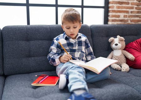 Photo for Adorable caucasian boy student drawing on notebook sitting on sofa at home - Royalty Free Image