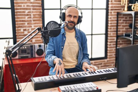 Téléchargez les photos : Jeune homme chauve musicien souriant confiant jouer du piano au studio de musique - en image libre de droit