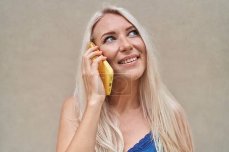 Téléchargez les photos : Jeune femme blonde souriante confiante parlant sur le smartphone sur fond blanc isolé - en image libre de droit