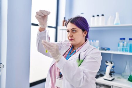 Téléchargez les photos : Young beautiful plus size woman scientist pouring liquid on test tube at laboratory - en image libre de droit