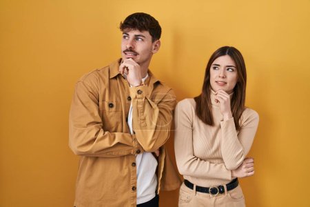 Photo for Young hispanic couple standing over yellow background thinking worried about a question, concerned and nervous with hand on chin - Royalty Free Image