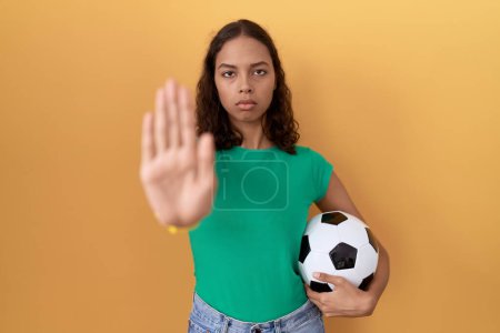 Téléchargez les photos : Jeune femme hispanique tenant le ballon faire arrêter de chanter avec la paume de la main. expression d'avertissement avec geste négatif et sérieux sur le visage. - en image libre de droit
