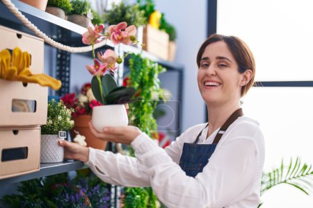 Téléchargez les photos : Young woman florist smiling confident holding plant at florist shop - en image libre de droit