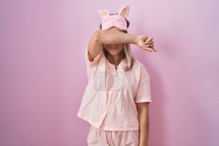 Photo for Blonde caucasian woman wearing sleep mask and pajama covering eyes with arm, looking serious and sad. sightless, hiding and rejection concept - Royalty Free Image