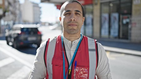 Photo for Young hispanic man volunteer wearing vest looking serious at street - Royalty Free Image