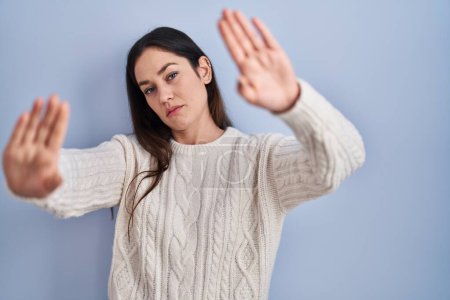 Téléchargez les photos : Jeune femme brune debout sur fond bleu faisant cadre en utilisant les mains paumes et les doigts, perspective de la caméra - en image libre de droit