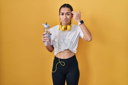 Photo for Young south asian woman wearing sportswear drinking water shooting and killing oneself pointing hand and fingers to head like gun, suicide gesture. - Royalty Free Image