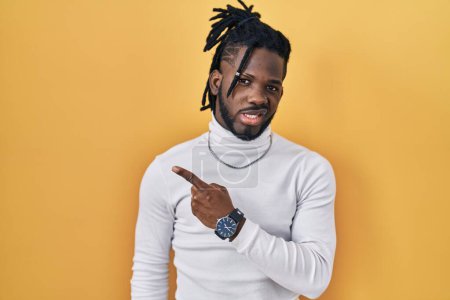 Photo for African man with dreadlocks wearing turtleneck sweater over yellow background pointing aside worried and nervous with forefinger, concerned and surprised expression - Royalty Free Image