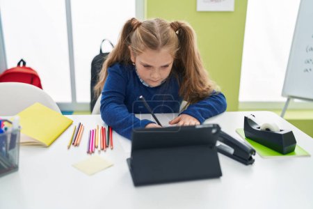 Photo for Adorable blonde girl student using touchpad writing notes at classroom - Royalty Free Image