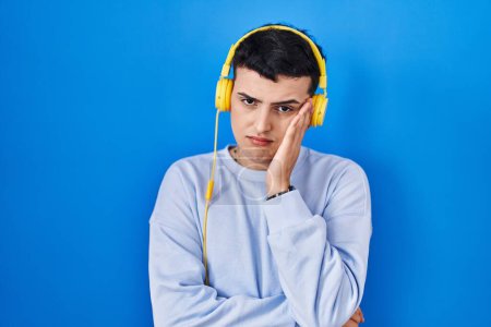 Foto de Persona no binaria escuchando música usando auriculares pensando que se ve cansada y aburrida con problemas de depresión con los brazos cruzados. - Imagen libre de derechos