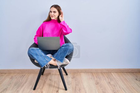 Photo for Young hispanic girl working using computer laptop smiling with hand over ear listening an hearing to rumor or gossip. deafness concept. - Royalty Free Image