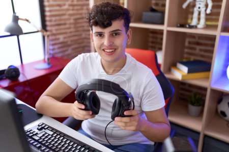 Téléchargez les photos : Non binary man streamer sitting on table holding headphones at gaming room - en image libre de droit