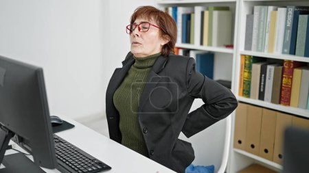 Téléchargez les photos : Mature hispanique femme professeur d'université à l'aide d'un ordinateur avec mal de dos à la bibliothèque universitaire - en image libre de droit