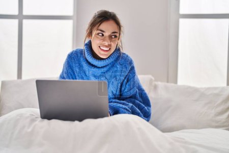 Foto de Young beautiful hispanic woman using laptop sitting on bed at bedroom - Imagen libre de derechos